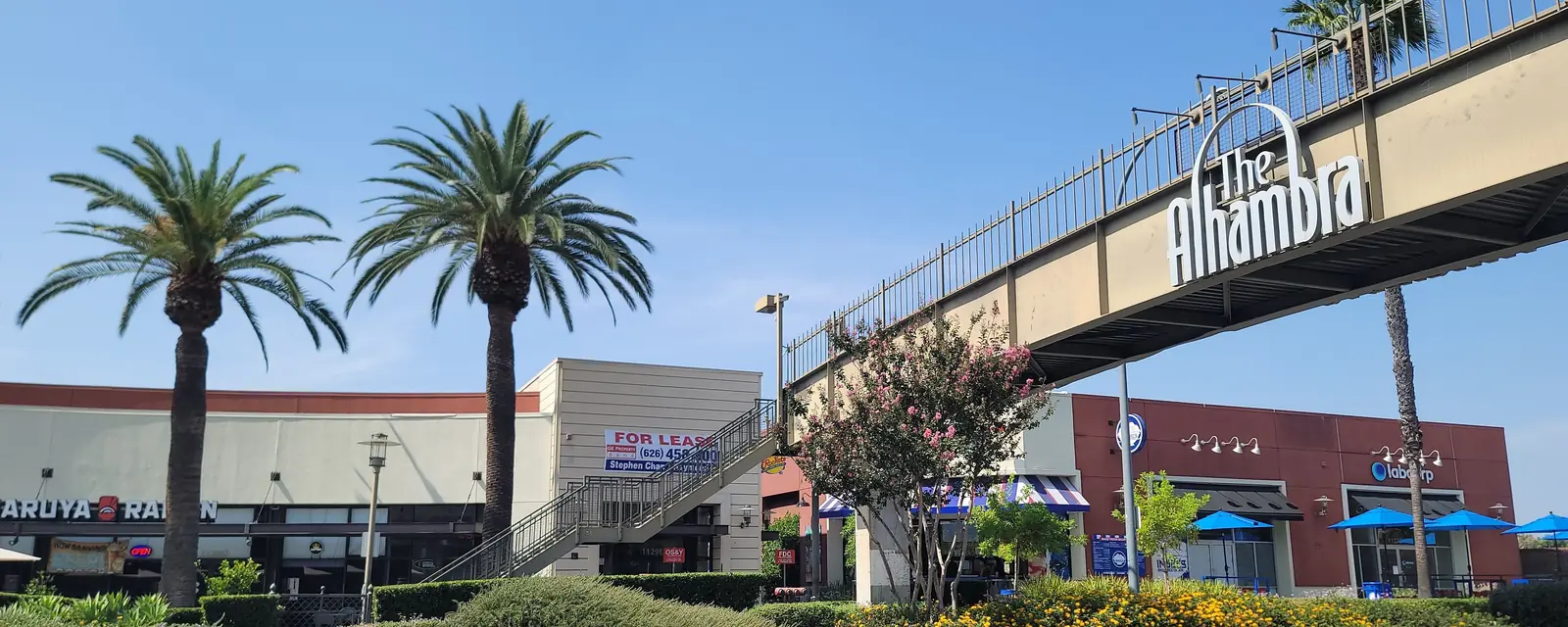 The “The Alhambra” sign on a pedestrian bridge above a palm-lined street in Alhambra
